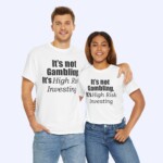 A man and a woman stand together, smiling and wearing white "It's Not Gambling It's High Risk Investing Shirt" with bold black text.