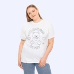 A smiling person with long, light brown hair wears the Thank God I’m Gay Shirt, a cheerful white tee featuring a teddy bear, hearts, and flowers, posed against a light background.