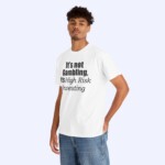 A young man stands against a plain light background wearing the "It's Not Gambling It's High Risk Investing Shirt," which features the slogan boldly printed in black.