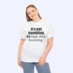 A smiling woman with long, light brown hair wears the "It's Not Gambling It's High Risk Investing Shirt," featuring the phrase in black text. She stands with one hand at her side and the other on her hip.