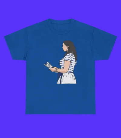 The Indianapolis Colts Carlie Irsay Gordon Shirt is a blue tee with an illustration of a woman with long brown hair in a blue-and-white striped top and white skirt, holding papers on a bright blue background.
