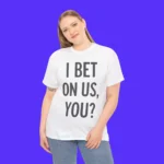 Against a solid purple background, a woman smiles softly wearing the I Bet On Us You Shirt—a white tee with bold black text: I BET ON US, YOU? Paired with light blue jeans, she poses with one hand on her hip.