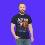 A bearded man, hand in pocket, smiles while wearing the Angry Runs Bills James Cook III Shirt—a navy blue tee with “Angry Runs,” an illustrated player, and James Cook III—set against a bright blue background.
